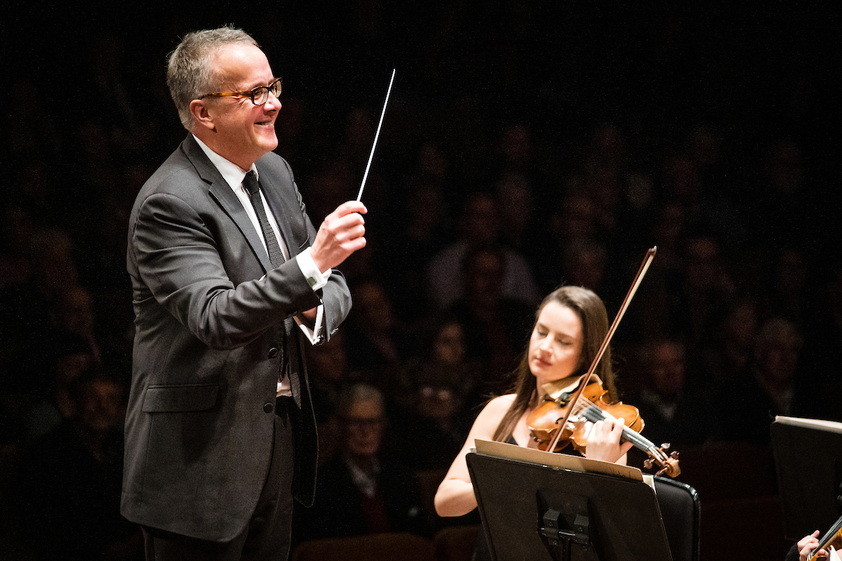 Music Director Marc Taddei conducting from the podium, concertmaster Amalia Hall (seated) performing at the Michael Fowler Centre in Wellington.